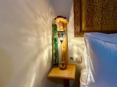a lamp on a side table next to a bed at Riad Noor Medina in Fès