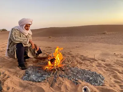 a woman sitting next to a fire in the desert at Dar Yaya & excursion - M'Hamid El Ghizlane in Mhamid