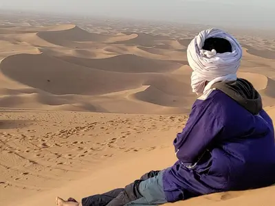 a man sitting in the sand in the desert at Dar Yaya & excursion - M'Hamid El Ghizlane in Mhamid