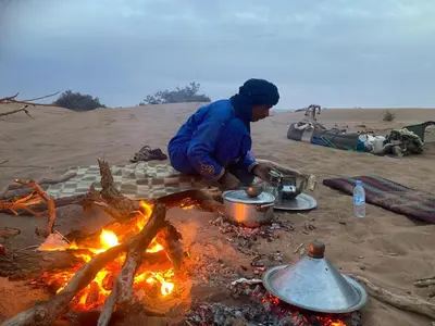a woman cooking over a camp fire in the desert at Dar Yaya & excursion - M'Hamid El Ghizlane in Mhamid