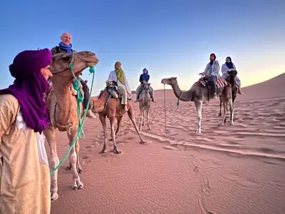 a group of people riding on camels in the desert at Dar Yaya & excursion - M'Hamid El Ghizlane in Mhamid