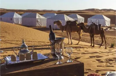 a table in the middle of the desert with camels at Merzouga Spirit Luxury Camp in Merzouga