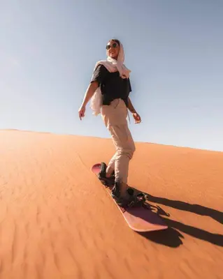 a woman riding a snowboard in the desert at Merzouga Spirit Luxury Camp in Merzouga