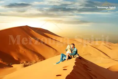 a couple sitting on top of a sand dune in the desert at Merzouga Spirit Luxury Camp in Merzouga