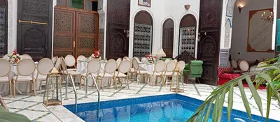 a room with a pool with tables and chairs next to a swimming pool at Palais Chahd Luxury in Fès