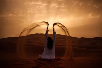 a woman sitting in the desert with her hands in the air at Merzouga desert Luxury Camp in Merzouga