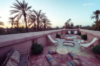 a patio with chairs and a table and palm trees at L'Ma Lodge in Skoura