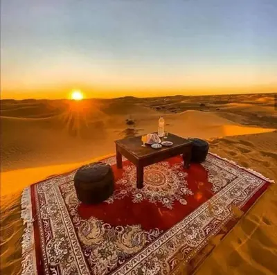 a table in the middle of a desert with the sunset at Merzouga Nomad Camp in Merzouga