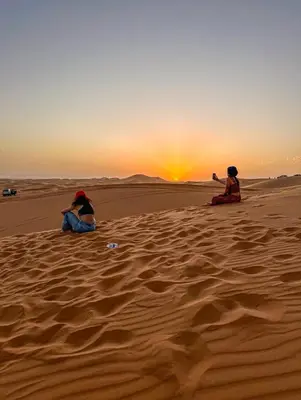 two people sitting in the desert watching the sunset at Merzouga Nomad Camp in Merzouga