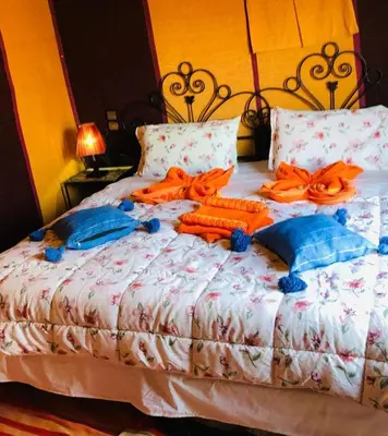 a bed with orange robes and pillows on it at Merzouga Nomad Camp in Merzouga