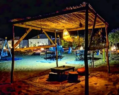 a pavilion with tables and chairs in the sand at night at Rachid Luxury Camp in Merzouga
