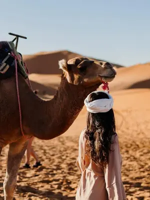 a woman standing next to a camel in the desert at Desert Bliss Luxury Camp in Merzouga