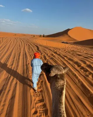 a man and a camel walking in the desert at Desert Bliss Luxury Camp in Merzouga