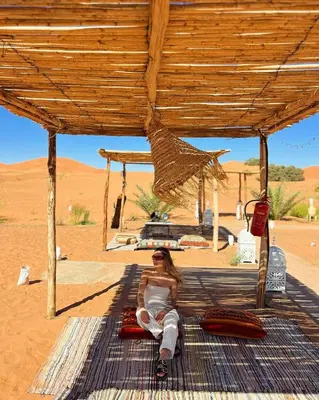 a woman sitting on a blanket in the desert at Desert Bliss Luxury Camp in Merzouga
