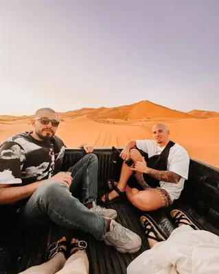 three men sitting in the back of a truck in the desert at Desert Bliss Luxury Camp in Merzouga