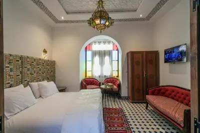 a bedroom with a bed and two chairs and a chandelier at DARIF's Riad & Spa in Fès