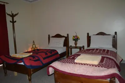 a bedroom with two beds and a table with a lamp at Hotel Almanader in Boumalne