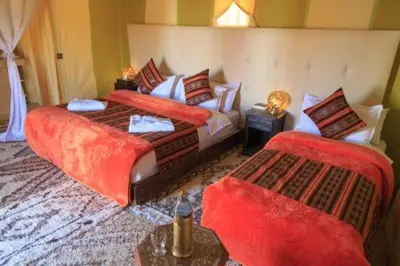 a bedroom with two beds with red sheets and a couch at Merzouga Luxury Tent in Merzouga