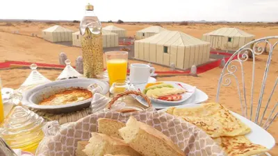 a table with plates of food on a table in the desert at Merzouga Luxury Tent in Merzouga