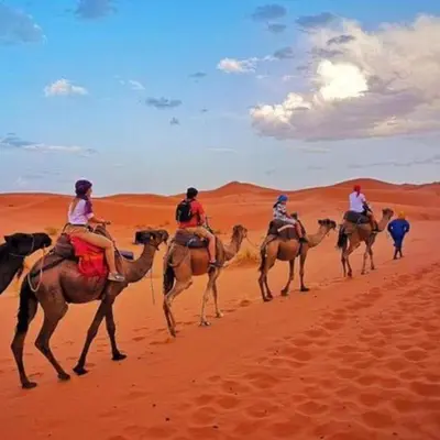 a group of people riding camels in the desert at Merzouga Luxury Tent in Merzouga