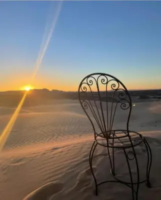 a chair sitting in the sand in the desert at Africa Magic Camp in Merzouga