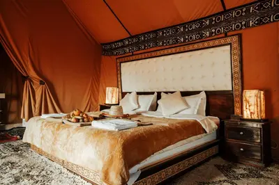 a bedroom with a large bed with an orange wall at Sahara Luxury Camp in Merzouga
