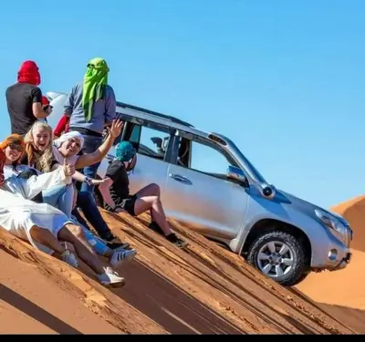 a group of people sitting on the sand next to a car at Sahara Luxury Camp in Merzouga