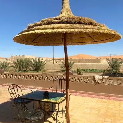 a table and chair under a large straw umbrella at Dar Hassi Labied Merzouga in Hassilabied