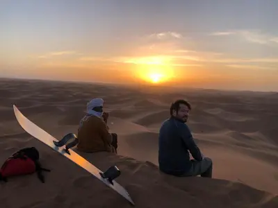 three people sitting in the desert watching the sunset at Desert Chegaga Luxury Camp in El Gouera