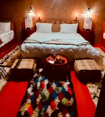 a bedroom with a large bed with a colorful rug at Desert Chegaga Luxury Camp in El Gouera