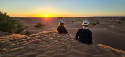 a man and woman sitting on a rock in the desert watching the sunset at Desert Chegaga Luxury Camp in El Gouera