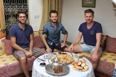 three men sitting on a couch with a table of food at Dar Fatimazahra in Fès
