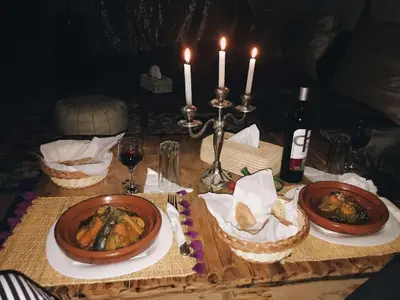 a wooden table with two plates of food and candles at Camel Experience Camp in Merzouga