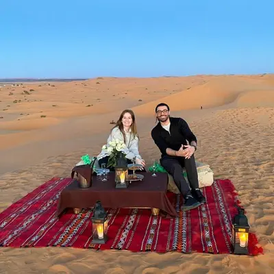 a man and woman sitting on a table in the desert at Camel Experience Camp in Merzouga