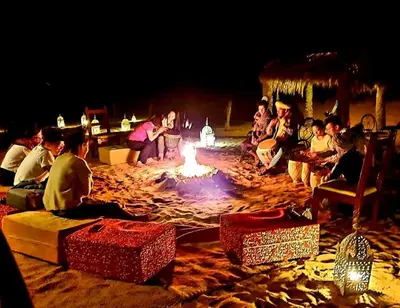 a group of people sitting around a fire pit at night at Camel Experience Camp in Merzouga