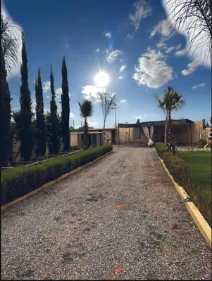 a driveway with trees and a building and the sun at Les jardins d’ailleurs in Marrakech
