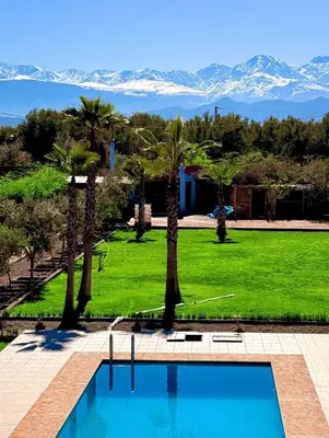 a swimming pool with palm trees and mountains in the background at Maison Dar Zarka in Aghmat