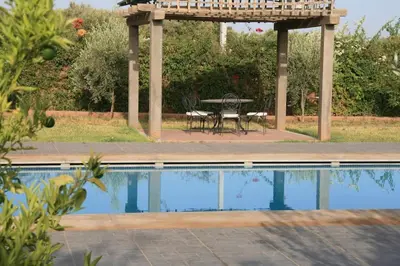 a pergola with a table and chairs next to a swimming pool at Maison Dar Zarka in Aghmat