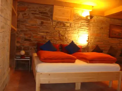 a bed with red pillows in a room with a stone wall at Kasbah Hotel Ait Omar in Nkob