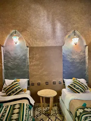 a room with two beds and a table in it at chez aubazine in Merzouga
