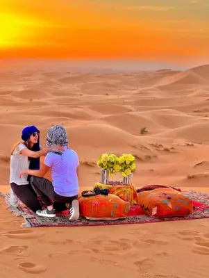 two people sitting on a blanket in the desert at Merzouga Luxurious Camp in Merzouga