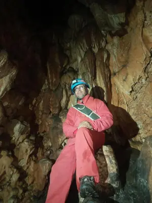 a man is sitting on a rock in a cave at Gite Ain Bechar in Taza