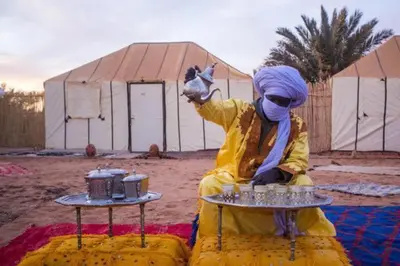 a person in a yellow suit holding up a table at Hamada Activities Luxury Camp in Merzouga