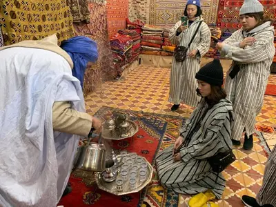 a group of people in a shop with a man pouring tea at Hamada Activities Luxury Camp in Merzouga