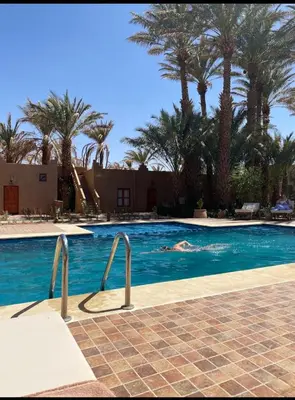 a person swimming in a swimming pool with palm trees at Zagora Oasis Lodge & Desert Excursions in Zagora