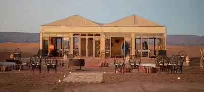 a building in the middle of the desert with tables and chairs at Erg chegaga Daya Luxury Camp - Sahara Desert Stay in Mhamid