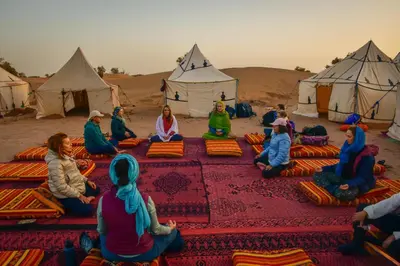 a group of people sitting in front of tents in the desert at Mhamid Nomad Camp in Mhamid