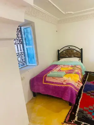 a bedroom with a bed with a purple blanket and a window at Riad et Restaurant chez Alilouch in Nkob