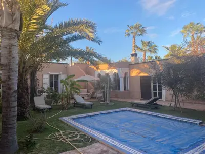 a swimming pool in front of a house with palm trees at Exceptionnelle Villa riad avec cuisinière-Piscine chauffée-Fibre internet in Marrakech