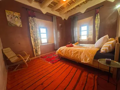 a bedroom with a bed and a table and two windows at KASBAH ALTAÏR in Kalaat MGouna